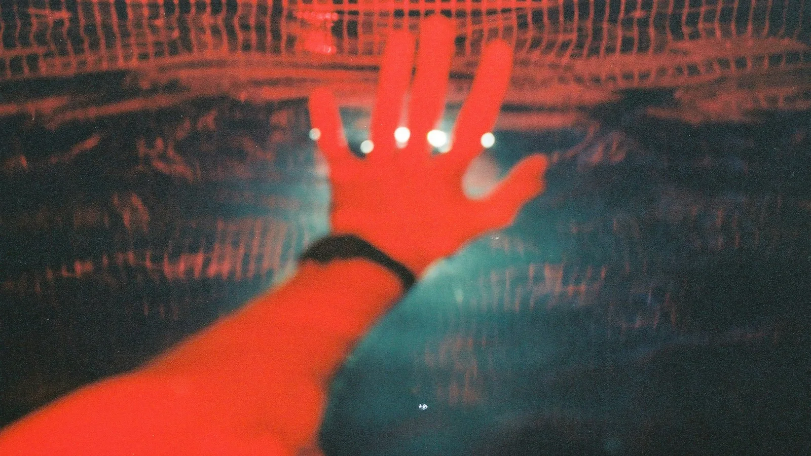 A raised hand lit red, pressed against glass